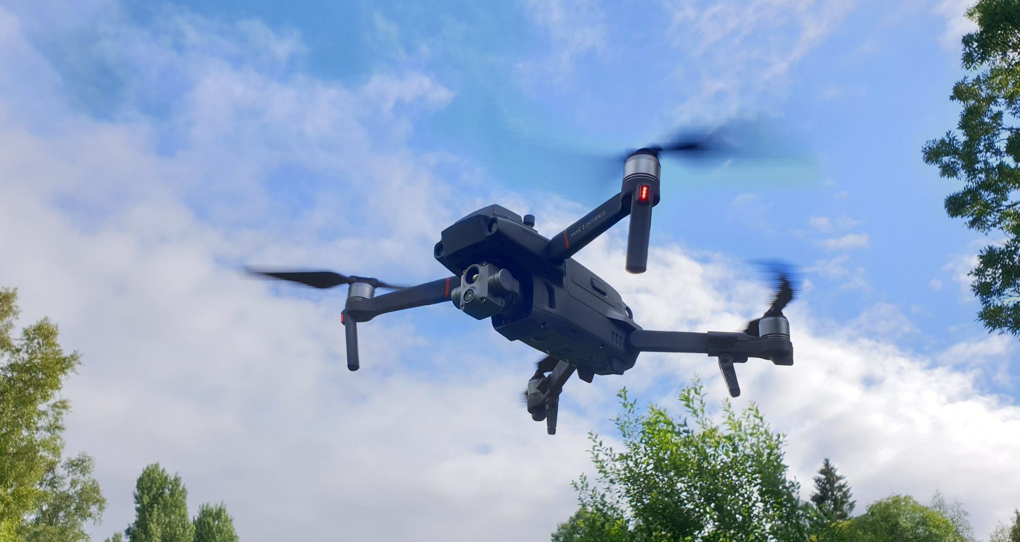 en drönaren som flyger i luften, trädtoppar skymtar framför en molnig himmel